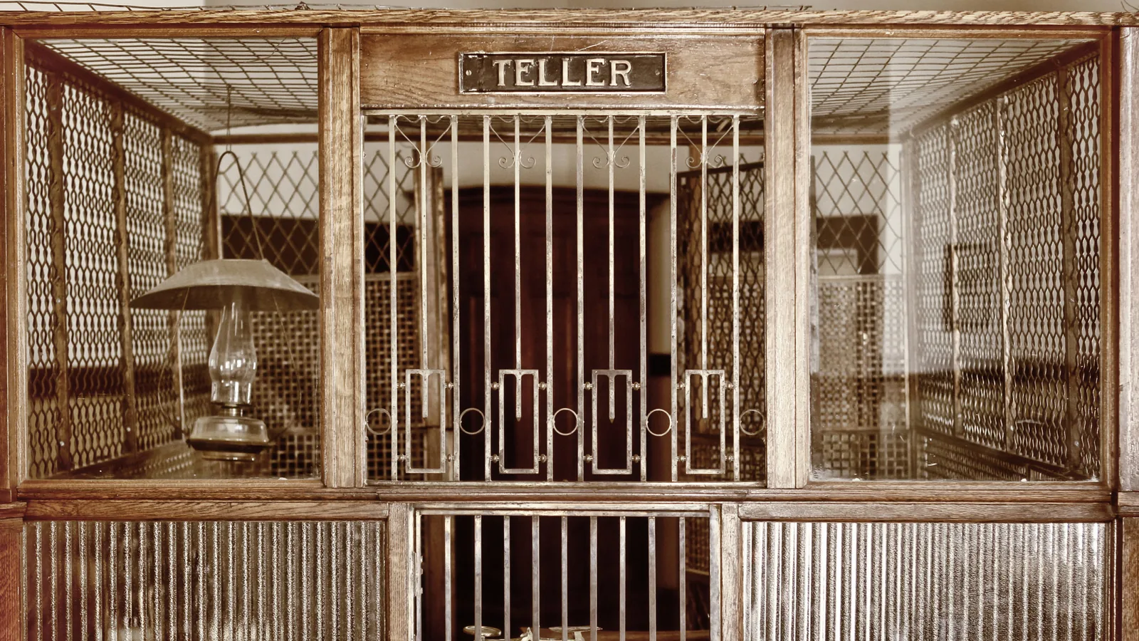Vintage brass and oak bank teller window cage with a TELLER sign, evoking the era before ATMs and online banking
